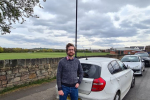 Alexander Stafford stands near parked vehicles on road