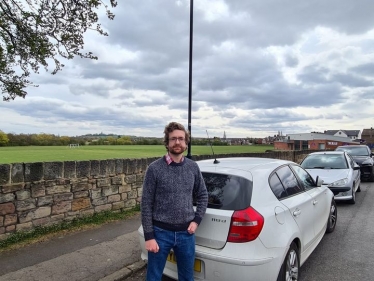 Alexander Stafford stands near parked vehicles on road