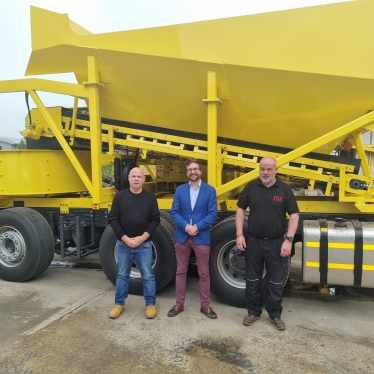 Alexander Stafford MP stands in front of a digger at Mixamate in Dinnington with two other people